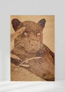 Pyrography of a black panther on a tree branch with 3 leaves to one side
