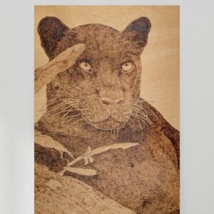 Pyrography of a black panther on a tree branch with 3 leaves to one side
